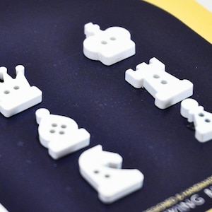 Può includere: Bottoni bianchi a forma di pezzi degli scacchi, tra cui re, regina, torre, alfiere, cavallo e pedone. I bottoni sono disposti su una superficie blu scuro. Ideali per progetti di cucito.