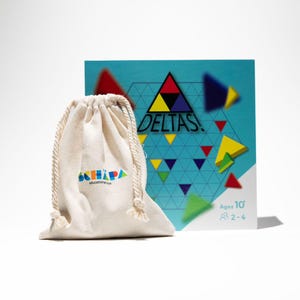 Pode incluir: Uma caixa de jogo azul e branca com o título "DELTAS!" e um design geométrico colorido. A caixa está ao lado de uma bolsa de cordão branco com o logotipo "SKHAPA" impresso nela.
