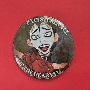 May include: A round button with an illustration of a person with white face paint and black hair. The button reads "PAVI STEALS ALL OF THE HEARTS!" and features a cartoon heart.