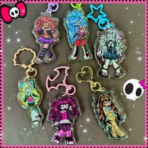 May include: Collection of colorful acrylic keychains featuring cartoon characters. Each keychain has a unique design with vibrant colors, including pink, blue, green, and purple. The keychains have gold-colored metal rings and clasps.