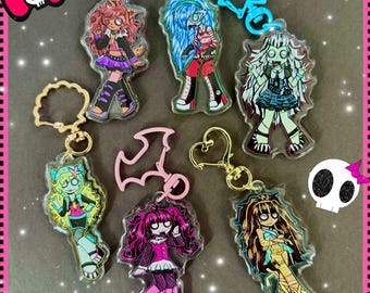 May include: Collection of colorful acrylic keychains featuring cartoon characters. Each keychain has a unique design with vibrant colors, including pink, blue, green, and purple. The keychains have gold-colored metal rings and clasps.