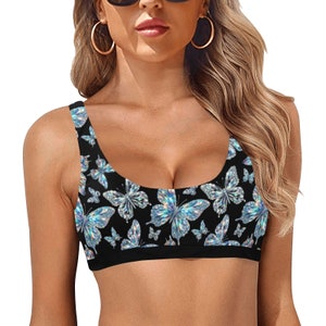 May include: Black sports bra with a repeating pattern of iridescent butterflies. The butterflies have a shimmering, multi-colored effect against the black background. The bra has a scoop neckline and a black band at the bottom.