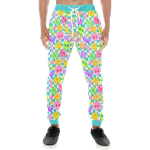 May include: Jogger pants with a colorful pattern of smiley faces, hearts, lightning bolts, butterflies, and alien heads on a checkered background. The pants have a turquoise waistband and cuffs, and a white drawstring.