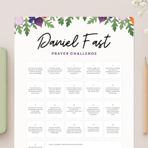May include: A light green Bible beside a "Daniel Fast Prayer Challenge" chart. The chart has a floral border and a list of prayer prompts. A pencil and a small vase of white flowers are also on the table.