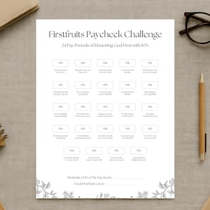 May include: A white printed sheet titled "Firstfruits Paycheck Challenge" with a floral border. The sheet has boxes with text like "10%" and phrases about honoring God. A pen, glasses, and a notebook are on the table.