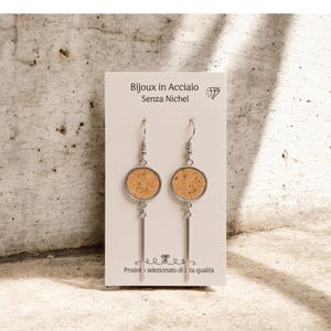 May include: A pair of earrings with a circular cork design and a silver bar. The earrings are displayed on a white card with the text "Bijoux in Acciaio Senza Nichel".