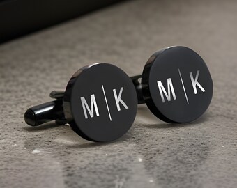 May include: A pair of black cufflinks with a silver engraved design. The cufflinks feature the initials "M|K" on each side.