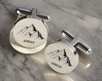 May include: Silver cufflinks with a mountain range design and the name "Adrian" engraved on each cufflink.