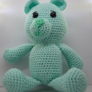 May include: A crocheted light blue teddy bear with black eyes and a green nose.