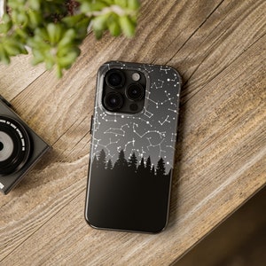 May include: Black phone case with a constellation design and a silhouette of a forest at the bottom. The case has a clear back and a black frame.
