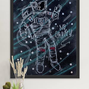 Puede incluir: Lámina artística enmarcada en negro que representa un astronauta dibujado con líneas blancas flotando en el espacio. El traje espacial tiene detalles rojos. El fondo es oscuro con puntos blancos y rayas turquesas. Las palabras "NO GRAVITY" están escritas en blanco.