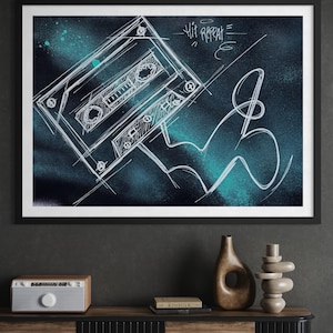 Op de afbeelding: Een ingelijste kunstdruk met een witte schets van een cassettebandje en de tekst "Hit Repeat" op een donkerblauwe en blauwgroene achtergrond. Het kunstwerk zit in een zwarte lijst.