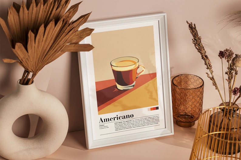 May include: A white framed print with a minimalist illustration of a cup of coffee and the word "Americano" in bold text. The print has a brown, orange, and yellow color scheme.