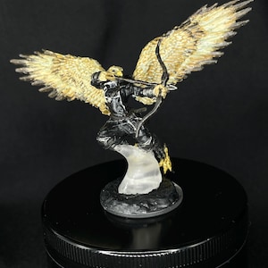 May include: A miniature figurine of a winged archer, painted in black and gold, with a bow and arrow, standing on a clear plastic base.