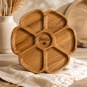 May include: A circular wooden serving tray with six distinct compartments arranged in a flower-like pattern. The centre of the tray features the engraved name Amelia above a small heart symbol. The wood grain is visible throughout the surface.