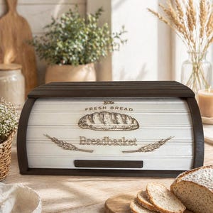 Op de afbeelding: Een houten broodtrommel met een donkerbruin frame en een wit voorpaneel. Het voorpaneel toont de woorden "Fresh Bread" en "Breadbasket" met een illustratie van een brood en tarwearen. Gesneden brood ligt op een houten snijplank.