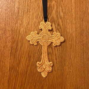 May include: A gold embroidered cross with intricate details hangs from a black ribbon. The cross is a religious symbol and would make a beautiful addition to any home.