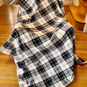 May include: A white, black, and red plaid fleece throw blanket draped over a chair. The blanket is soft and cozy, perfect for snuggling up on the couch.