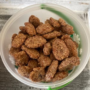 Könnte beinhalten: Ein durchsichtiger Plastikbehälter gefüllt mit Pecan-Hälften, überzogen mit braunem Zuckerguss.