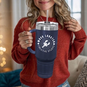 May include: A blue and stainless steel tumbler with a black handle and a white logo that says "Mock Lobster Creative Studio" with a lobster graphic.