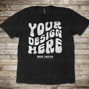 May include: Black t-shirt with a white graphic that says "YOUR DESIGN HERE" in a retro, psychedelic font. The text is slightly distressed, giving it a vintage look.