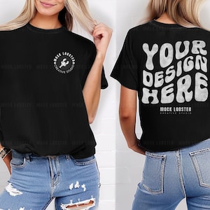 Puede incluir: Camiseta negra con gráficos blancos. La parte delantera presenta un pequeño logotipo circular con una langosta y el texto "MOCK LOBSTER CREATIVE STUDIO". La parte trasera muestra "YOUR DESIGN HERE" en una fuente retro, con el nombre del estudio debajo.