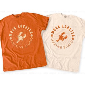 May include: Two t-shirts, one orange and one off-white, each featuring a circular logo with a lobster illustration and the text "MOCK LOBSTER CREATIVE STUDIO". The shirts are short-sleeved and appear to be made of a soft material.