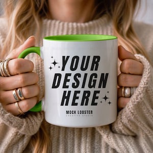May include: White ceramic mug with a green rim and handle. The mug has the text "YOUR DESIGN HERE" in black lettering and the words "MOCK LOBSTER CREATIVE STUDIO" in smaller black lettering.