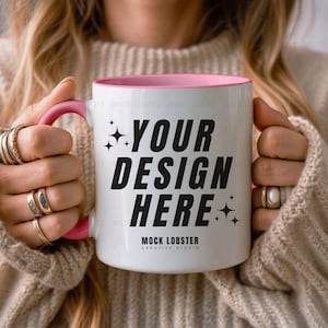 Op de afbeelding: Een witte keramische mok met een roze rand en handvat. De mok heeft de tekst "YOUR DESIGN HERE" in zwarte letters en "MOCK LOBSTER CREATIVE STUDIO" in kleinere zwarte letters.