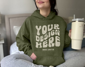 May include: A person wearing a green hooded sweatshirt with the text "YOUR DESIGN HERE" and the words "MOCK LOBSTER CREATIVE STUDIO" printed on the front. The person is holding a white travel mug with a straw.