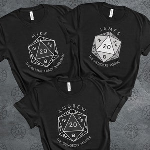 May include: Three black t-shirts with white text and a white graphic of a twenty-sided die. The text on the shirts reads "Mike the Batshit Crazy Barbarian", "James the Mediocre Rogue", and "Andrew the Dungeon Master".