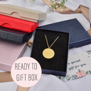 May include: A gold-colored pendant necklace with a round charm inside a navy blue gift box. The charm has an inscription. The image also shows several colorful gift boxes and a card that says "a special gift for you". The text "READY TO GIFT BOX" is also visible.