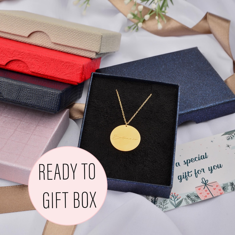 May include: A gold-colored pendant necklace with a round charm inside a navy blue gift box. The charm has an inscription. The image also shows several colorful gift boxes and a card that says "a special gift for you". The text "READY TO GIFT BOX" is also visible.