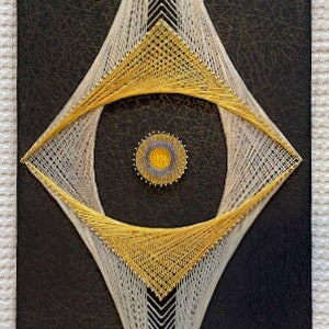 May include: A diamond-shaped string art piece with a white and gold thread design. The center of the diamond features a yellow circle with a blue and purple center.