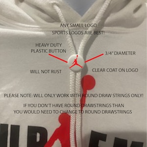 May include: White hooded sweatshirt with a red and black Supreme logo and a white drawstring. The drawstring has a heavy duty plastic button with a red Jumpman logo. The text "ANY SMALL LOGO SPORTS LOGOS ARE BEST!" is printed on the sweatshirt. The text "HEAVY DUTY PLASTIC BUTTON" is printed above the button. The text "WILL NOT RUST" is printed below the button. The text "3/4" DIAMETER" is printed above the button. The text "CLEAR COAT ON LOGO" is printed below the button. The text "PLEASE NOTE: WILL ONLY WORK WITH ROUND DRAW STRINGS ONLY! IF YOU DON'T HAVE ROUND DRAWSTRINGS THAN YOU WOULD NEED TO CHANGE TO ROUND DRAWSTRINGS" is printed below the logo.