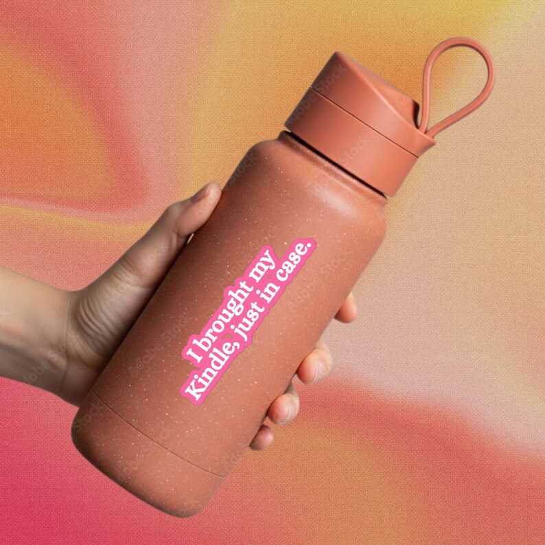 May include: A terracotta-colored water bottle with a speckled finish, a matching screw-top lid, and a flexible carrying loop. A rectangular sticker on the front features a pink background with white text that reads, I brought my Kindle, just in case.