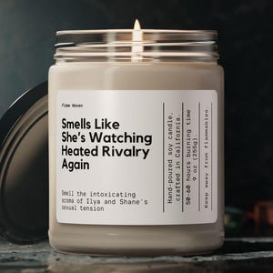 Può includere: Una candela di soia accesa in un barattolo di vetro trasparente con coperchio argentato. L'etichetta recita "Smells Like She's Watching Heated Rivalry Again". La candela è versata a mano in California, 50-60 ore di combustione, 255g.