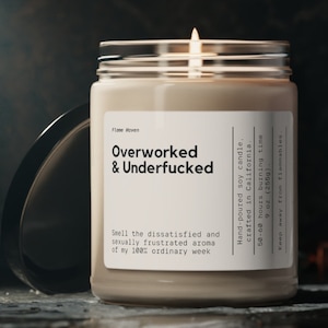 May include: A lit soy candle in a glass jar with a lid. The label reads "Overworked & Underfucked." The candle is hand-poured in California and has a 50-60 hour burn time. The jar is 255g.