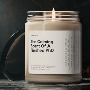 K&ouml;nnte beinhalten: Eine durchsichtige Glaskerze in einem Glas mit einem wei&szlig;en Etikett, auf dem "The Calming Scent Of A Finished PhD" steht. Die Kerze ist aus handgegossenem Sojawachs und in Kalifornien hergestellt. Sie hat eine Brenndauer von 50 bis 60 Stunden und wiegt 255 g (9 oz).