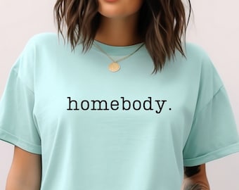 May include: A light blue t-shirt with the text "homebody." printed in black. The model is wearing the t-shirt with light blue denim shorts.