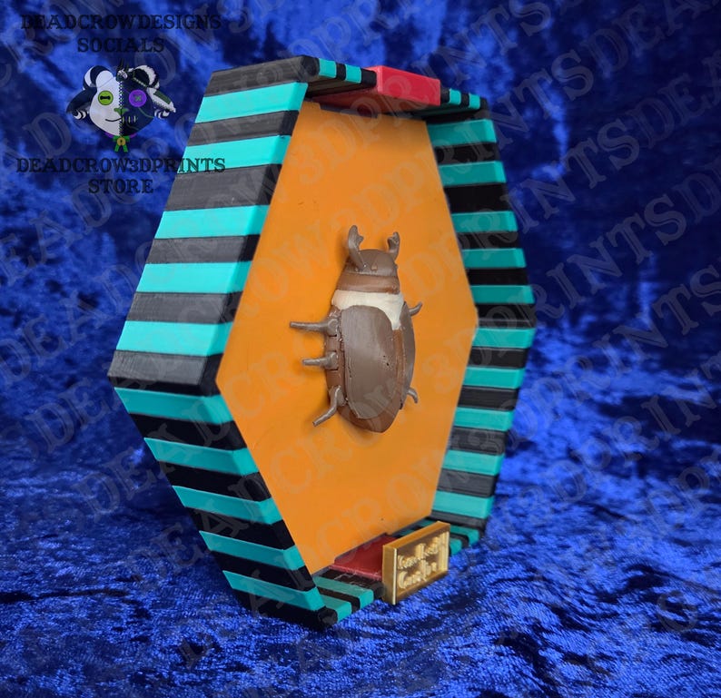 Puede incluir: Una vitrina geom&eacute;trica con una figura de escarabajo marr&oacute;n sobre un fondo naranja. La vitrina tiene detalles en negro, turquesa y rojo. El texto "DEADCROWDESIGNS SOCIALS" y "DEADCROW3DPRINTS STORE" son visibles.