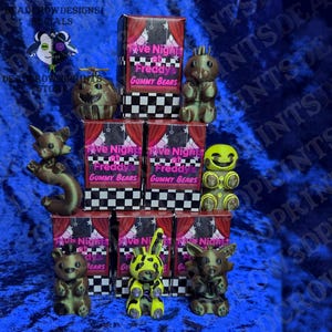 May include: An assortment of 3D-printed figurines and boxes. The boxes are red with the text "Five Nights at Freddy's Gummy Bears." The figurines include a bear, a fox, a rabbit, and other characters in various colors.