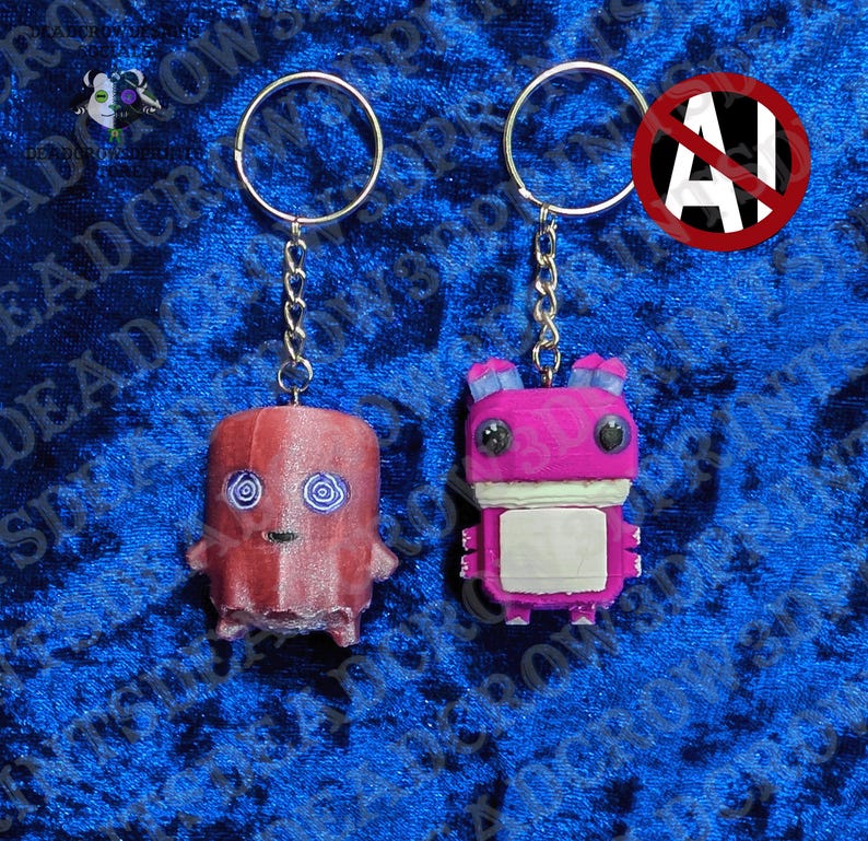 May include: Two keychains featuring stylized figures. The left figure is a reddish-brown ghost with blue spiral eyes. The right figure is a bright pink creature with large black eyes, blue ears, and a white rectangular chest panel, both on metal rings.