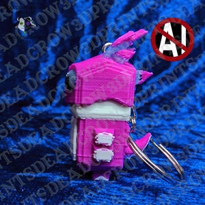 May include: A 3D-printed keychain featuring a stylized creature with a bright pink head and body, white accents on the chest and sides, and a metallic silver ring attached to the top. The figure has a blocky, geometric design with visible layer lines.