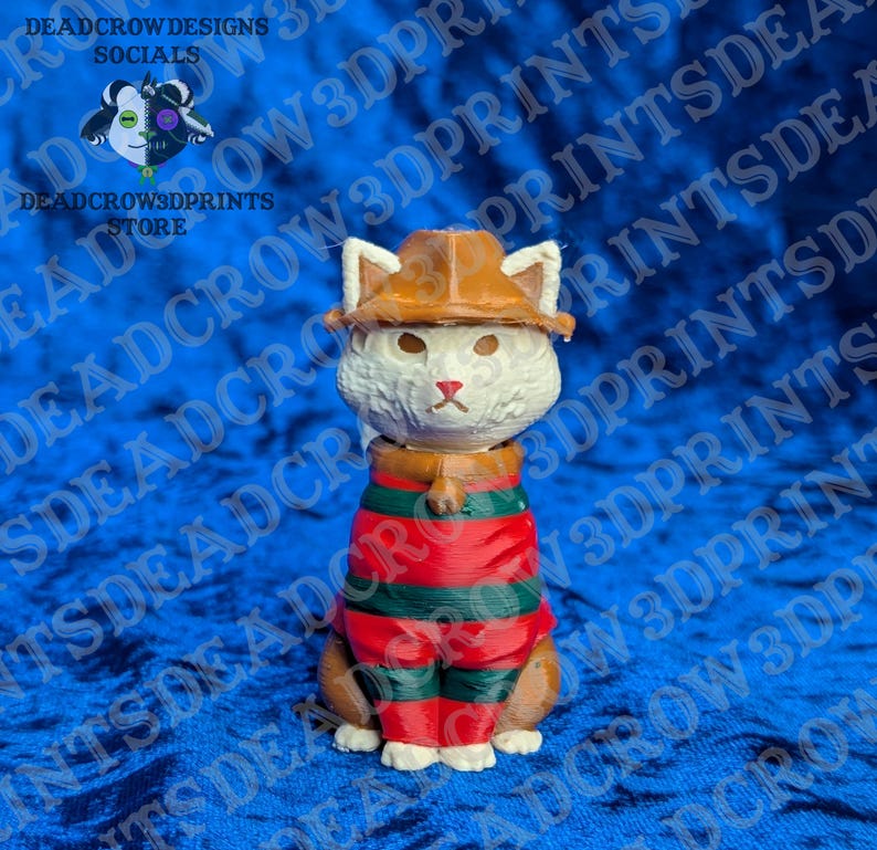 May include: A 3D printed figurine of a white cat wearing a brown fedora hat and a red and green horizontally striped sweater. The cat has pointed ears, a small red nose, and a neutral expression. The figure is rendered in a solid, matte finish.