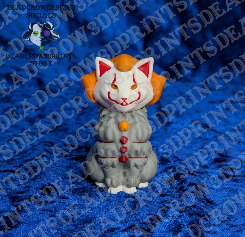 May include: A 3D printed figurine of a cat wearing a white mask with red markings and orange hair. The cat has a grey body with a small orange circular detail at the neck and three red vertical accents on its chest. The figure is standing upright.