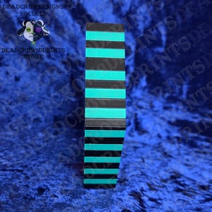 Puede incluir: Un objeto rectangular vertical con rayas horizontales alternas negras y turquesas. El objeto se encuentra sobre un fondo azul. El texto "DEADCROWDESIGNS SOCIALS" y "DEADCROW3DPRINTS STORE" son visibles.
