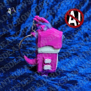 May include: A 3D-printed keychain featuring a blocky, stylized creature in vibrant magenta and white. The figure has a prominent magenta head with textured details, a white midsection, and a magenta tail. A metal split ring is attached to the top.