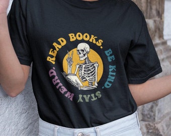 May include: Black t-shirt with a colorful graphic of a skeleton reading a book. The graphic says "Read Books. Stay Weird. Be Kind."