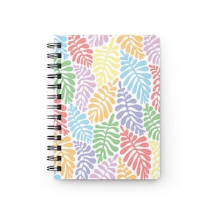 May include: A spiral bound notebook with a colorful leaf pattern. The leaves are in shades of pink, orange, yellow, green, blue, and purple.